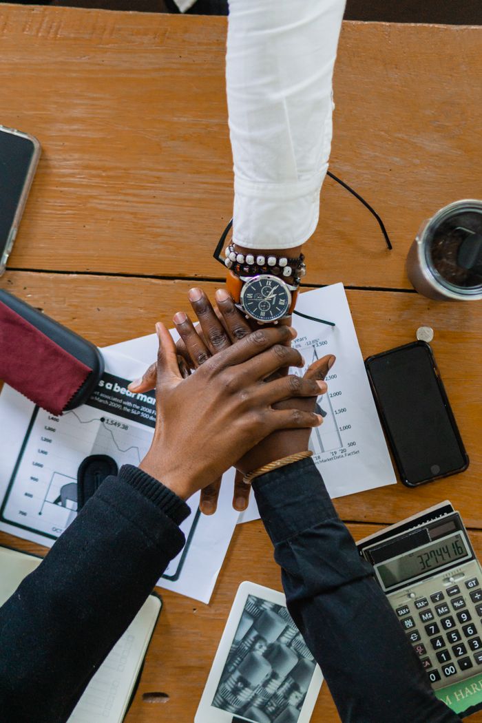 who-we-are Top view of diverse hands stacked on office desk, symbolizing teamwork and collaboration.
